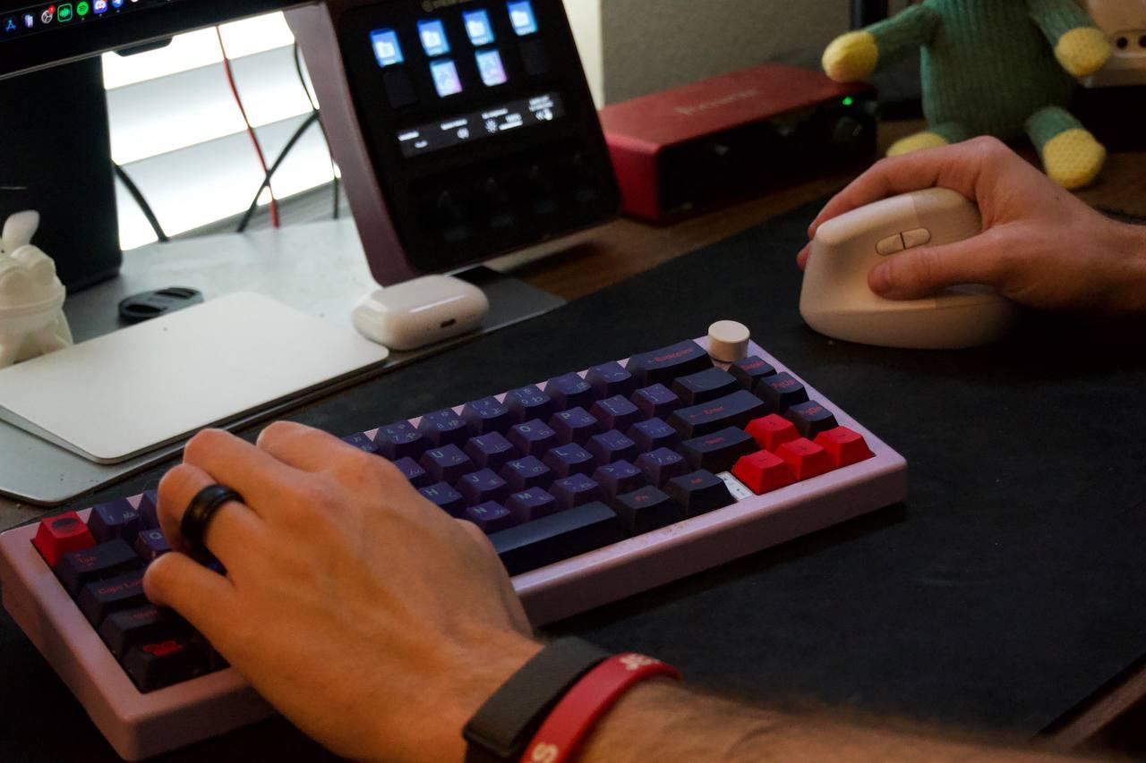 Tyler Delano at desk — pink mechanical keyboard, multi-monitor setup, studio monitors