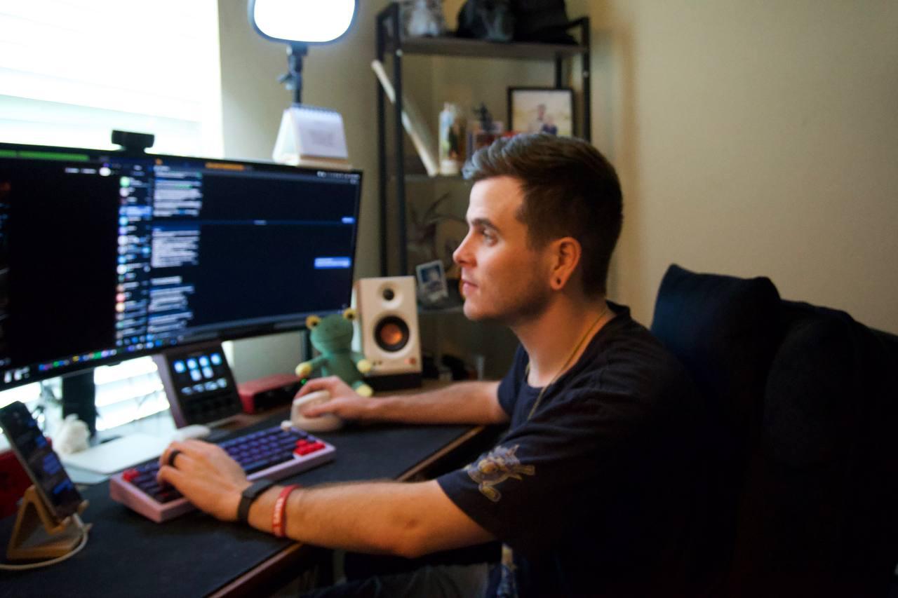 Tyler Delano at desk — multi-monitor setup, pink mechanical keyboard, ZV-E10 lighting